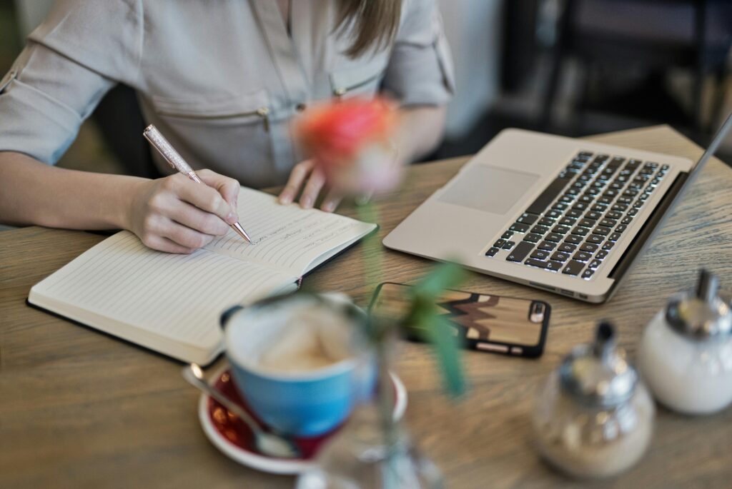 THE PICTURE DIFINES A LADY WRITING THE CONTENT IN NOTEPAD ,FREELANCE DIGITAL MARKETING SPECIALIST IN CONTENT MARKETING
